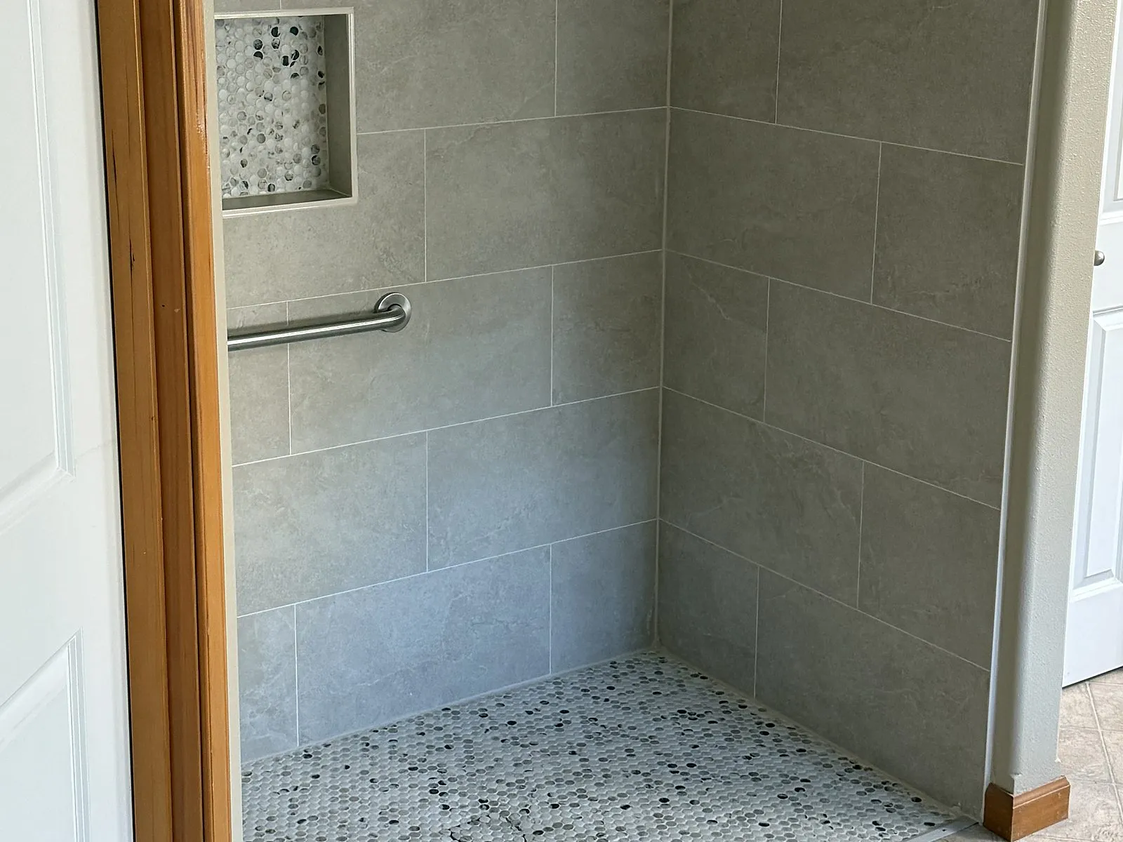 A curbless roll-in tile shower with a grab bar and a pebble mosaic floor