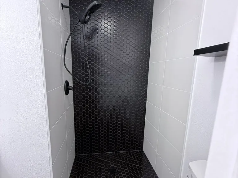 A walk-in shower tiled in black hexagon mosaic