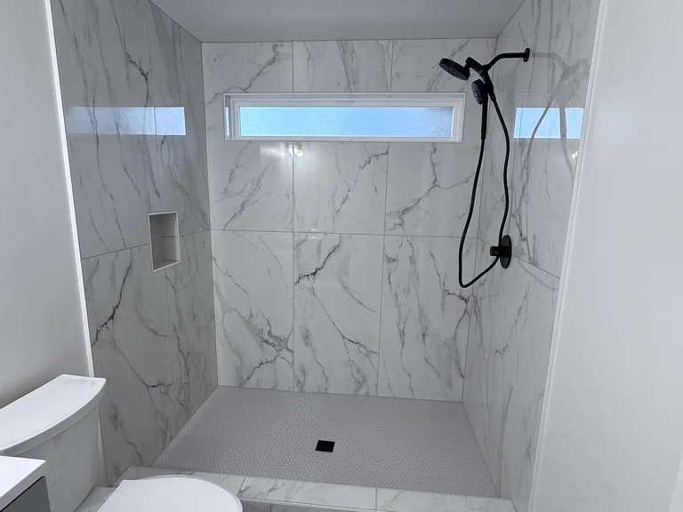 A marble-tiled walk-in shower with black fixtures and a clerestory window