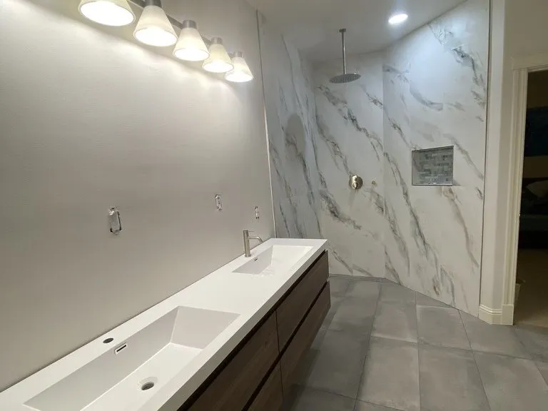 A long bathroom with a soaking tub, marble surround and a dark floating vanity