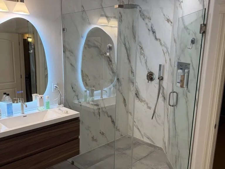 A marble shower beside an oval mirror and a timber vanity