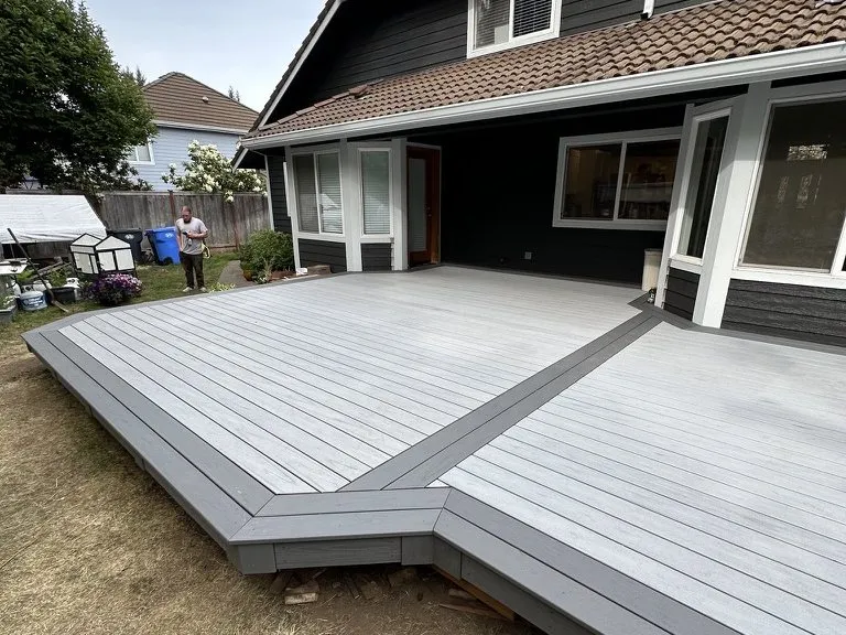 A finished grey deck with a light border, wrapping the back of the house