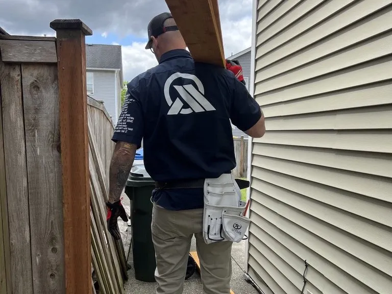 An All Home HX crew member carrying fence boards down the side of the house