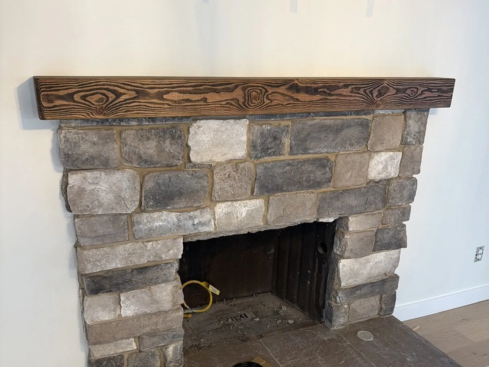 The same fireplace rebuilt in grey stone with a heavy timber mantel
