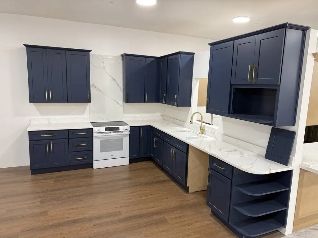 A kitchen with navy cabinets, white stone counters and a light plank floor
