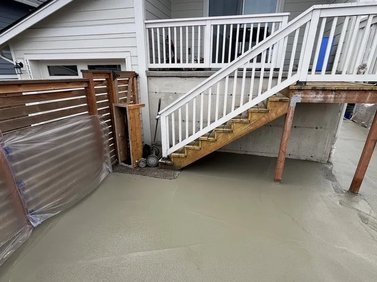 A poured concrete patio at the base of a deck stair