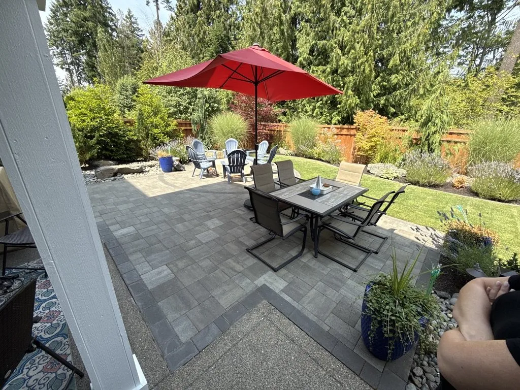 A paver patio with a table, chairs and a red umbrella