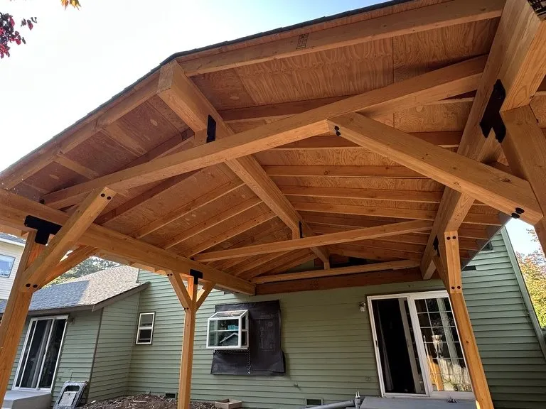 A heavy-timber pavilion with exposed rafters, built against the house