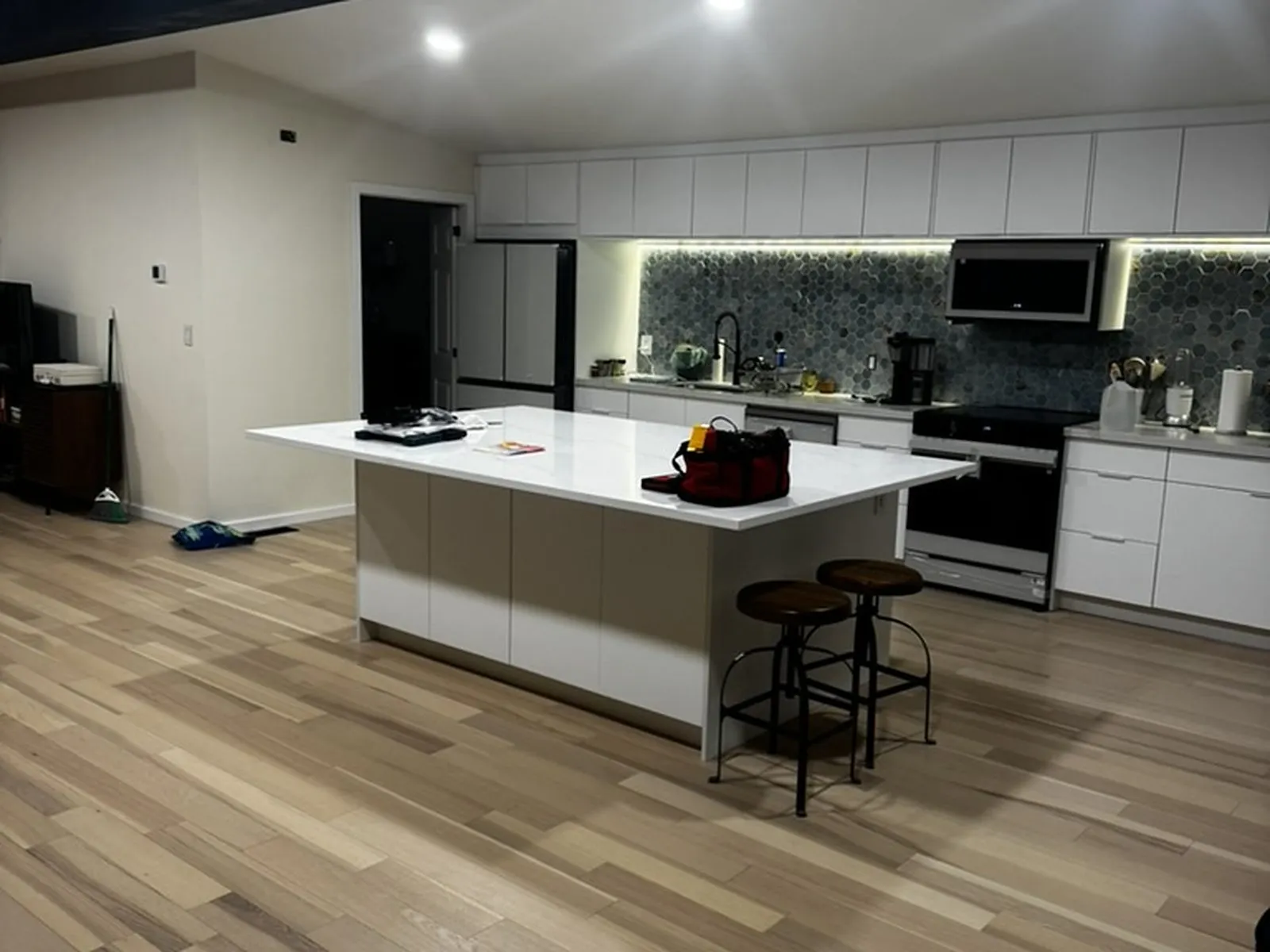 The same kitchen finished, with a white island, seating, a painted structural beam and plank flooring