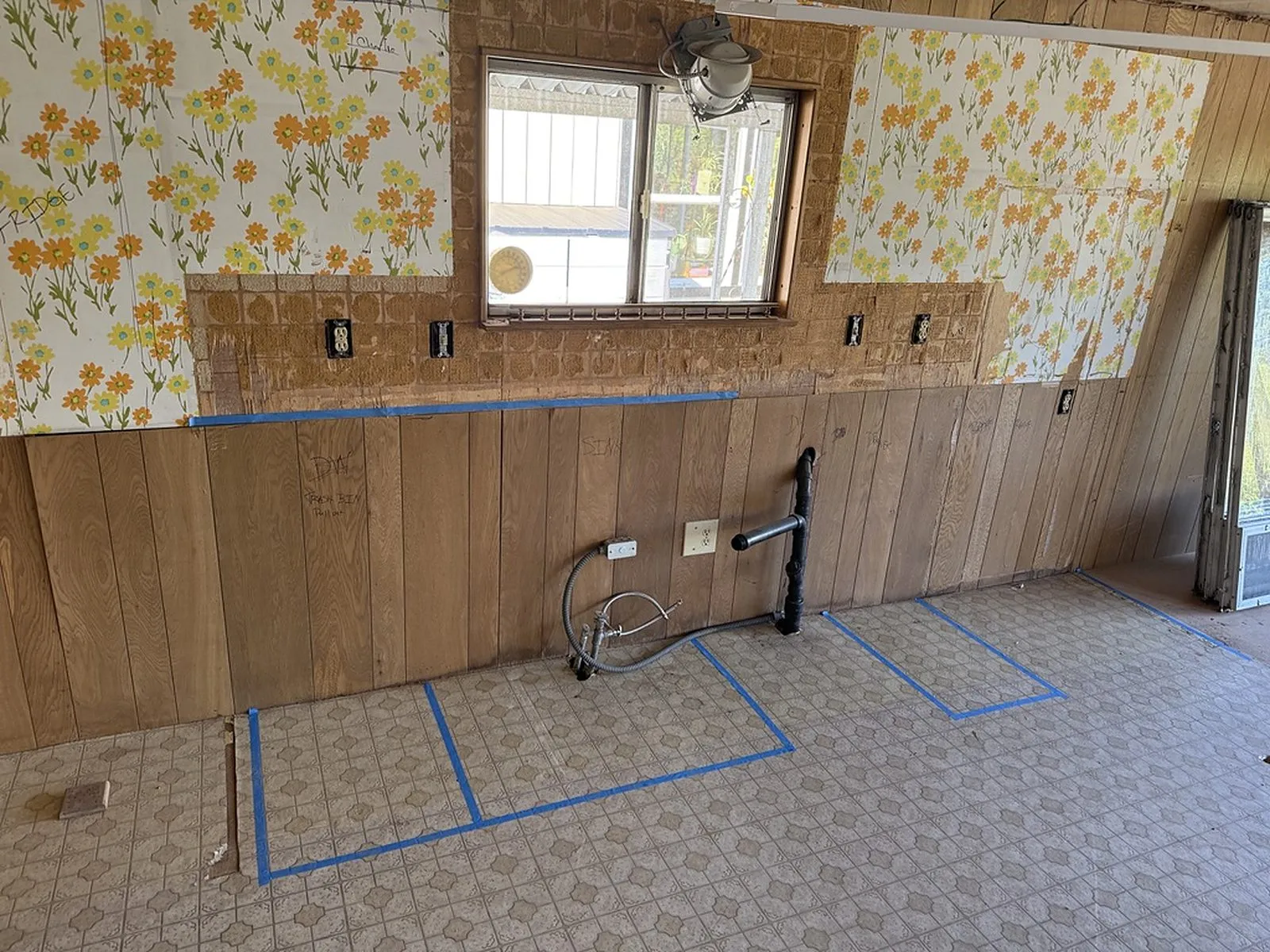 The original kitchen before work began, with floral wallpaper, wood panelling and sheet flooring